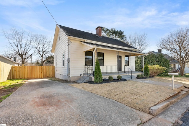 bungalow-style house with covered porch, a shingled roof, a chimney, and fence