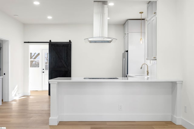 kitchen with a barn door, a peninsula, a sink, light wood-type flooring, and island exhaust hood