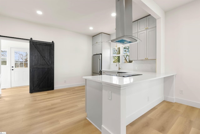 kitchen featuring a barn door, freestanding refrigerator, island exhaust hood, light countertops, and light wood-type flooring