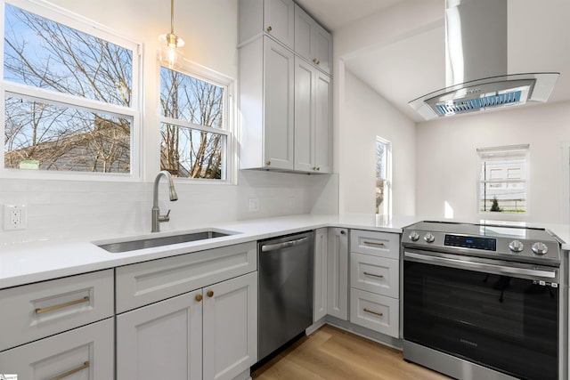 kitchen featuring island exhaust hood, stainless steel appliances, light countertops, light wood-style flooring, and a sink