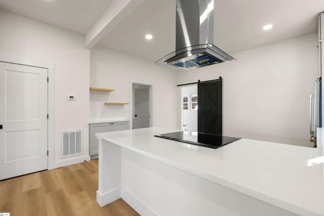 kitchen featuring a barn door, visible vents, black electric cooktop, ventilation hood, and light countertops