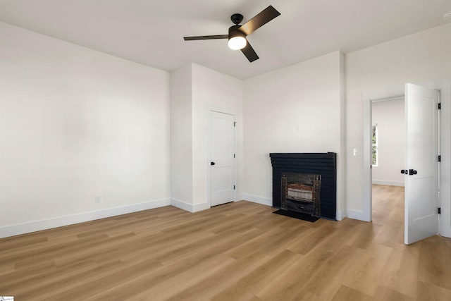 unfurnished living room featuring light wood-style floors, baseboards, ceiling fan, and a fireplace with flush hearth