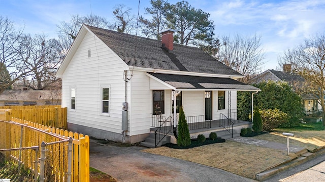 view of front of property with a porch, fence, a chimney, and a shingled roof