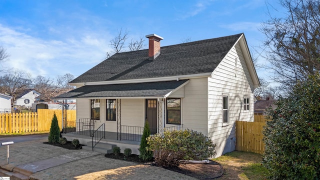 view of front of property with a chimney, fence, a porch, and roof with shingles