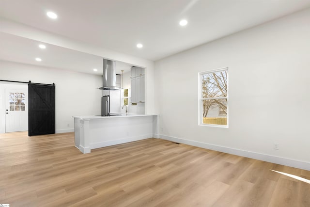 kitchen featuring a peninsula, a barn door, island range hood, and light wood-style flooring