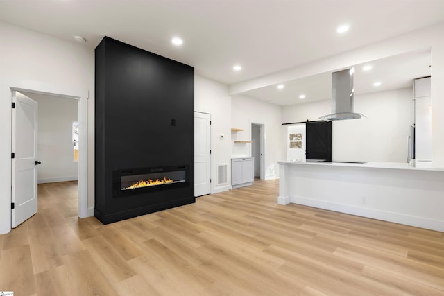 unfurnished living room featuring a large fireplace, a barn door, recessed lighting, and light wood-style floors