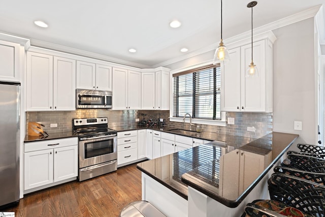 kitchen with a peninsula, appliances with stainless steel finishes, a sink, and white cabinetry