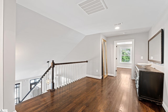 hall featuring baseboards, visible vents, dark wood finished floors, and an upstairs landing