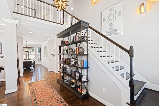 stairs featuring decorative columns, a towering ceiling, ornamental molding, wood finished floors, and baseboards