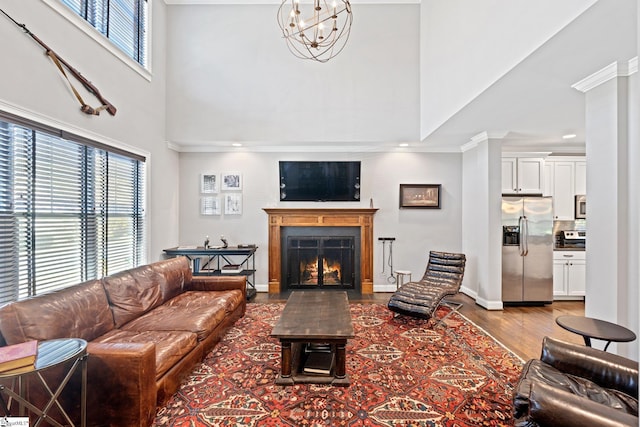 living area featuring a warm lit fireplace, wood finished floors, baseboards, ornamental molding, and an inviting chandelier