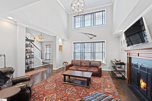 living room with an inviting chandelier, a fireplace with flush hearth, ornamental molding, wood finished floors, and stairs