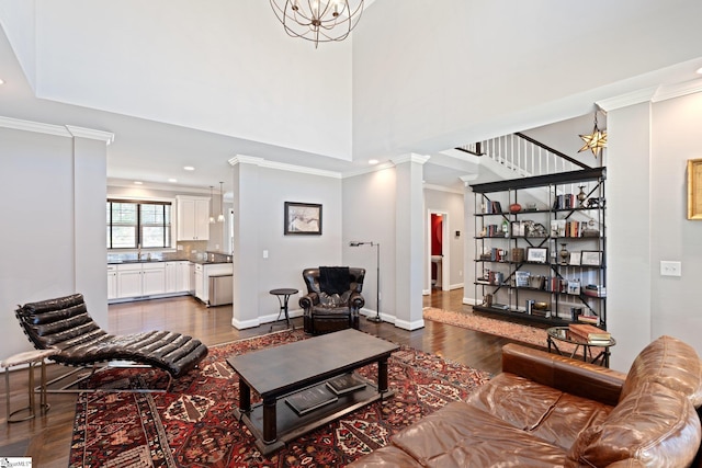 living area with a high ceiling, baseboards, dark wood-style floors, decorative columns, and crown molding