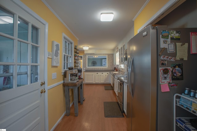 kitchen with light wood finished floors, white cabinets, ornamental molding, stainless steel appliances, and backsplash