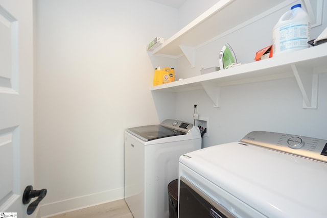 clothes washing area with light wood-type flooring, laundry area, washing machine and dryer, and baseboards