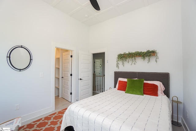 bedroom with a high ceiling, coffered ceiling, baseboards, and wood finished floors