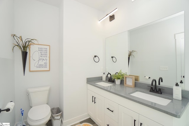 bathroom featuring toilet, double vanity, baseboards, and a sink