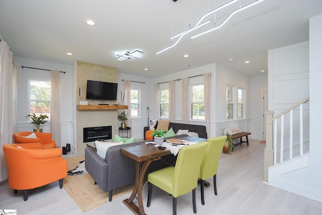 living room featuring a large fireplace, light wood-style flooring, stairs, and a wealth of natural light