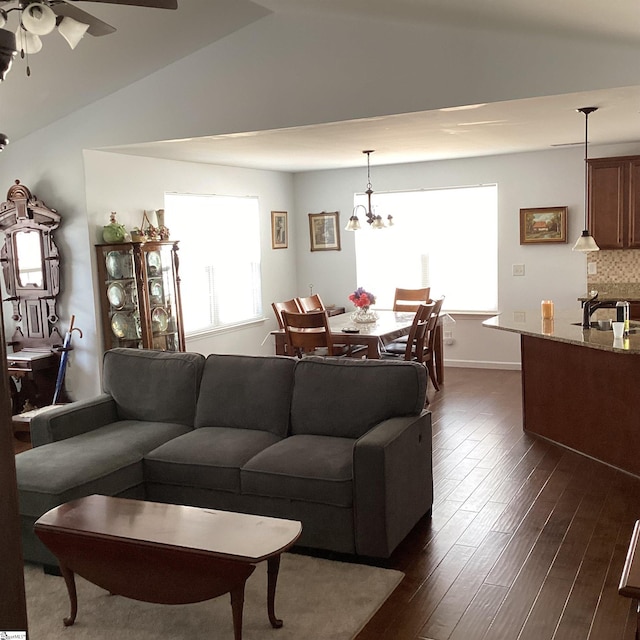 living area with dark wood-style floors, lofted ceiling, baseboards, and ceiling fan with notable chandelier