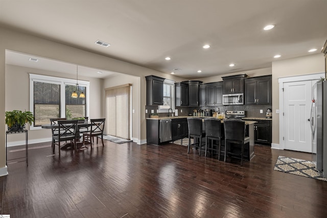 kitchen with stainless steel appliances, dark wood-type flooring, visible vents, decorative backsplash, and a kitchen bar