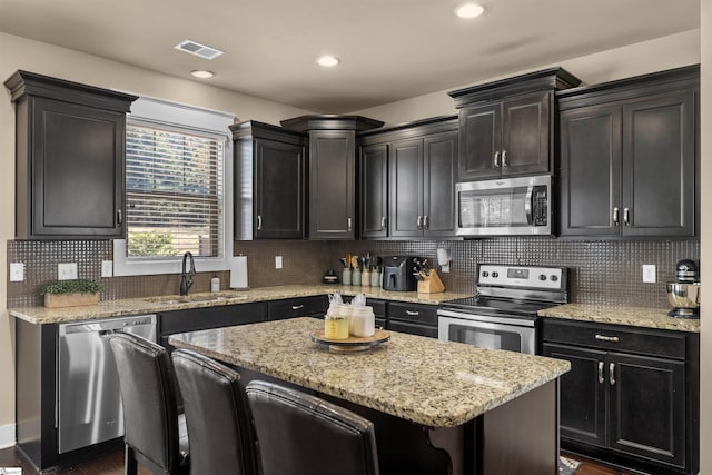 kitchen featuring visible vents, appliances with stainless steel finishes, a center island, a kitchen bar, and a sink