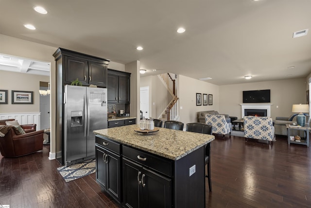 kitchen with a warm lit fireplace, open floor plan, dark wood finished floors, and stainless steel fridge with ice dispenser