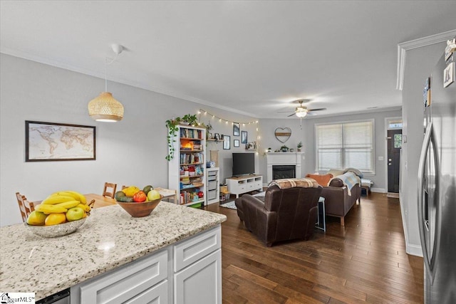 living room with a fireplace, dark wood-type flooring, a ceiling fan, ornamental molding, and baseboards