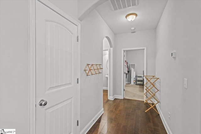 corridor featuring arched walkways, dark wood-style floors, visible vents, and baseboards