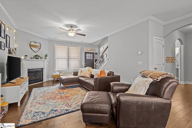 living area with arched walkways, ceiling fan, a fireplace, wood finished floors, and stairway