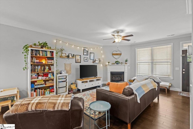 living area with crown molding, dark wood finished floors, a fireplace, ceiling fan, and baseboards