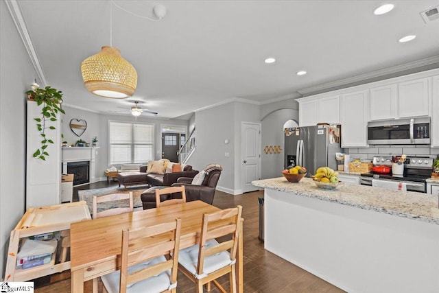 kitchen featuring appliances with stainless steel finishes, white cabinetry, ornamental molding, and a fireplace