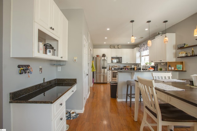 kitchen with white cabinets, appliances with stainless steel finishes, a kitchen breakfast bar, light wood-style floors, and a sink