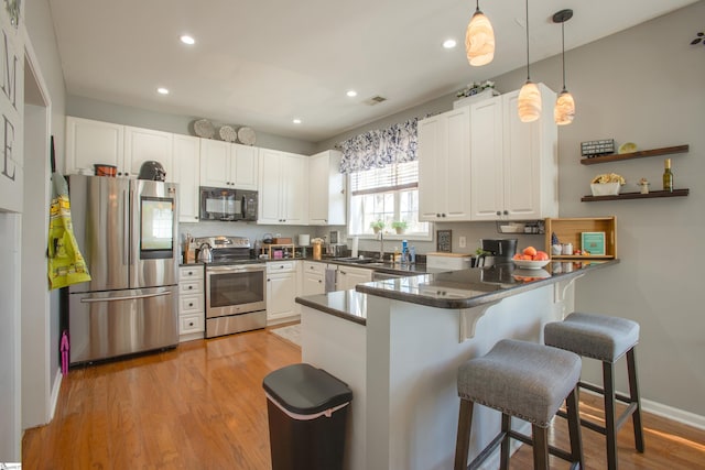 kitchen featuring a peninsula, dark countertops, light wood-style flooring, and appliances with stainless steel finishes