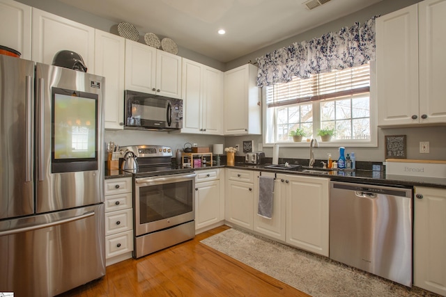 kitchen with recessed lighting, stainless steel appliances, a sink, white cabinets, and light wood-style floors