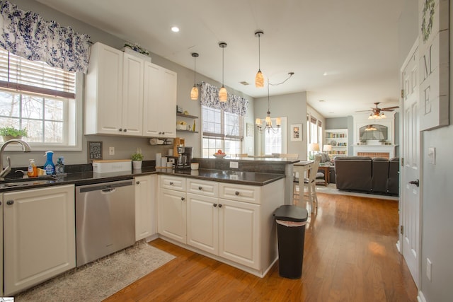 kitchen with light wood-style floors, open floor plan, a sink, dishwasher, and a peninsula