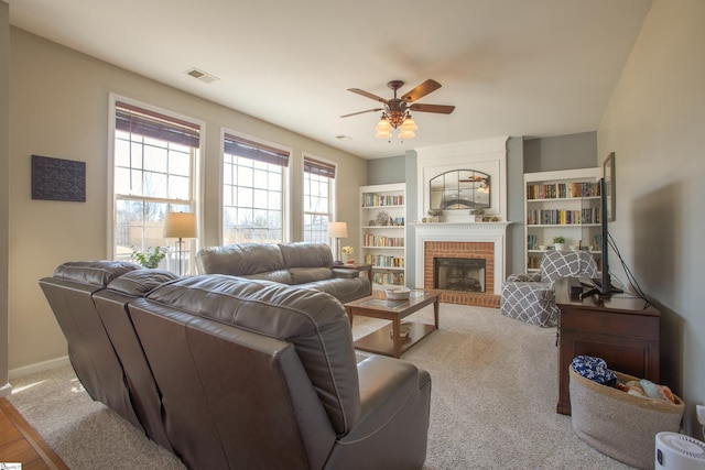 carpeted living room with ceiling fan, a fireplace, visible vents, and baseboards