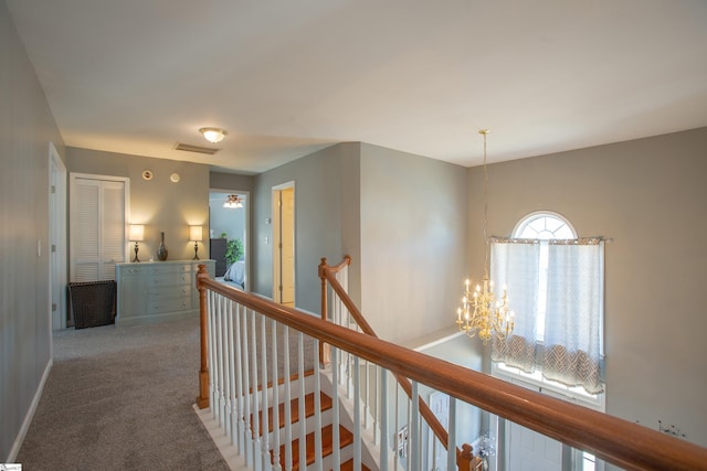 corridor with a notable chandelier, carpet floors, visible vents, baseboards, and an upstairs landing