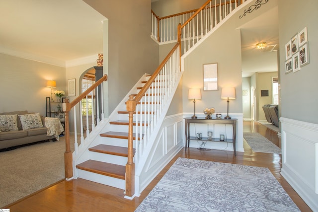 staircase with a towering ceiling, crown molding, and wood finished floors