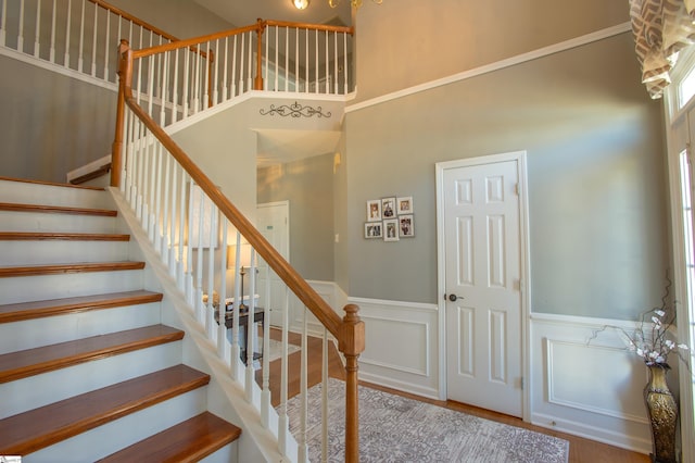 staircase featuring a wainscoted wall, a high ceiling, and wood finished floors