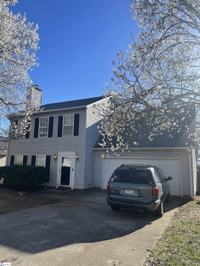 colonial home featuring driveway, a chimney, and an attached garage