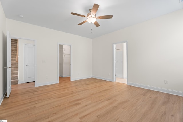 unfurnished bedroom with a ceiling fan, a closet, a walk in closet, light wood-style flooring, and baseboards