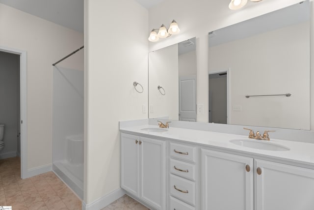bathroom featuring baseboards, a sink, a shower, and double vanity