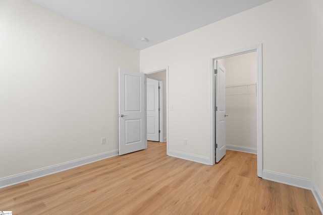 unfurnished bedroom featuring a spacious closet, baseboards, a closet, and light wood-type flooring