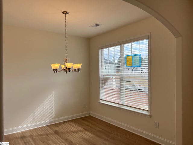 unfurnished dining area with arched walkways, wood finished floors, visible vents, and baseboards