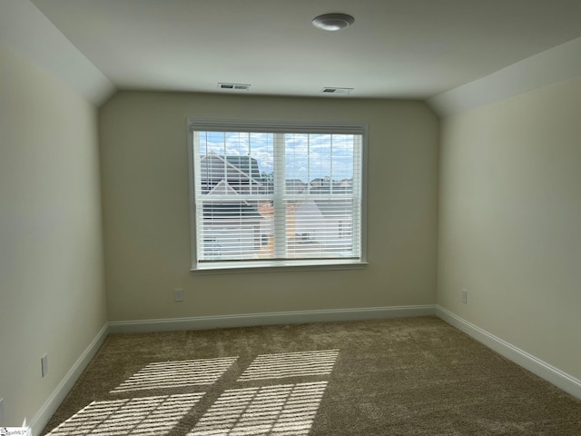 spare room featuring vaulted ceiling, carpet flooring, visible vents, and baseboards