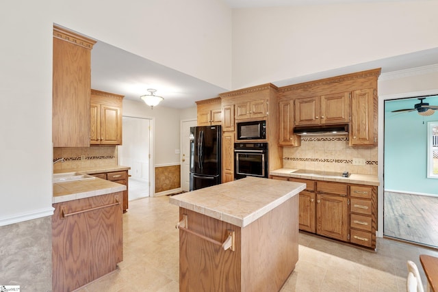 kitchen featuring tile counters, tasteful backsplash, a sink, under cabinet range hood, and black appliances