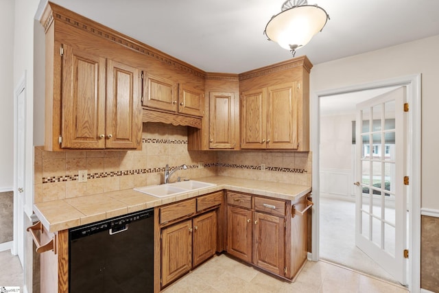 kitchen with tile countertops, a wainscoted wall, a sink, black dishwasher, and backsplash