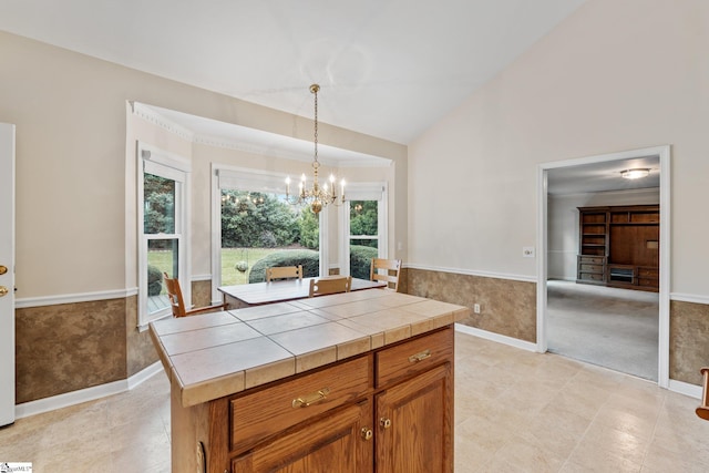 kitchen featuring tile countertops, a wainscoted wall, brown cabinets, an inviting chandelier, and pendant lighting