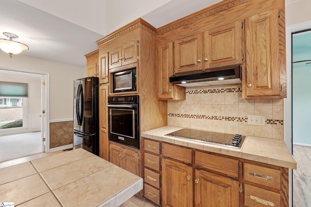 kitchen featuring backsplash, light tile patterned flooring, wainscoting, under cabinet range hood, and black appliances