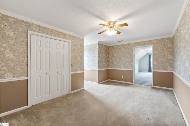 carpeted empty room with a textured ceiling, crown molding, visible vents, and wallpapered walls