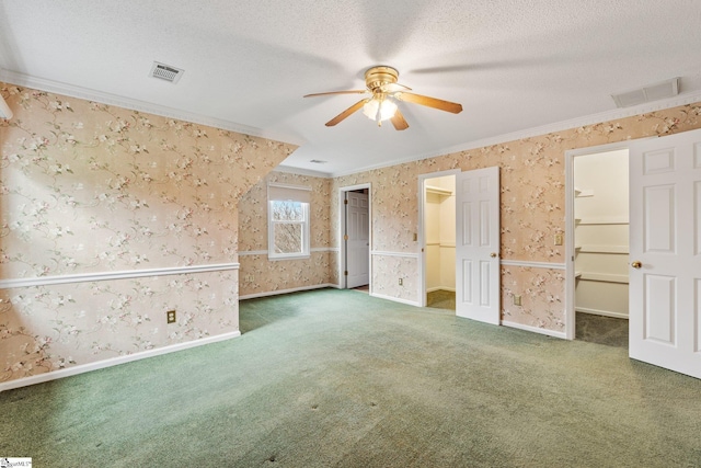 carpeted empty room with a textured ceiling, ceiling fan, visible vents, wallpapered walls, and crown molding